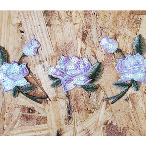 May include: Three purple and iridescent sequined rose appliques with green embroidered stems and leaves.