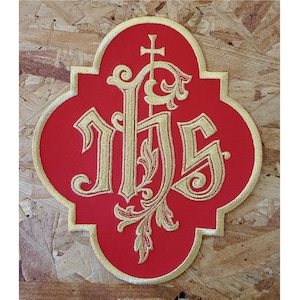 May include: A red embroidered patch with a gold 'IHS' monogram and a cross. The monogram is surrounded by ornate floral designs.