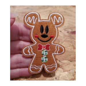May include: A gingerbread man with a red bow tie and green holly leaves. The gingerbread man is brown with white icing around the edges and has a smiling face with black eyes.