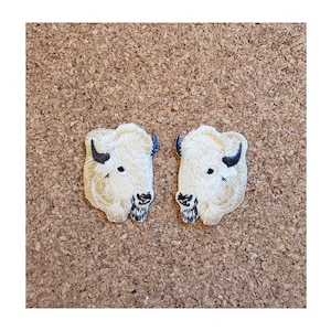 May include: Two white embroidered patches of a buffalo head, each with black horns and a black nose.