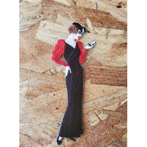 May include: Embroidered iron-on patch of a woman in a black dress with red sleeves and a black hat. She is holding a small mirror in her right hand.