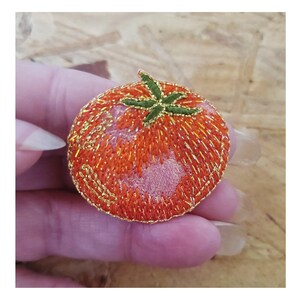 May include: A red embroidered tomato with gold stitching and green leaves. The tomato is about 2 inches in diameter.
