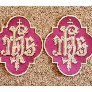 May include: Two gold embroidered patches with the letters "IHS" in a stylized font, surrounded by floral designs. The patches are on a red background and have a scalloped edge.
