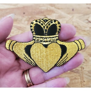 May include: Gold embroidered Irish Claddagh patch with a heart, two hands, and a crown. The hands are clasped together, holding a heart, and the crown is on top of the heart.