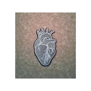 May include: White embroidered anatomical heart patch on a cork background.