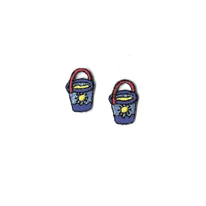 May include: Two small blue buckets with red handles and yellow flower designs. The buckets are embroidered with a yellow flower design.