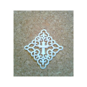 May include: White lace applique with a cross design. The applique is shaped like a diamond and has intricate details.