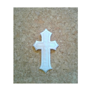 May include: White felt cross with a simple design. The cross is on a cork background.