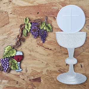 May include: Embroidered patches featuring religious and wine-related themes. One patch depicts a chalice with a host, and the other shows a bunch of grapes, a glass of wine, and grape vines. The patches are in shades of white, purple, green, and brown.