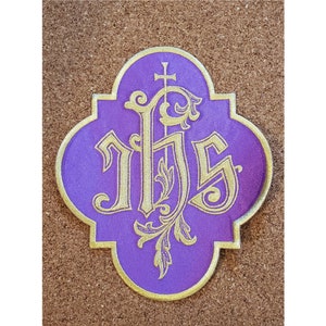 May include: A purple and gold religious icon with the letters "IHS" in a decorative font.