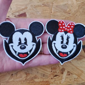 May include: Two embroidered patches featuring cartoon mouse characters. One patch depicts a male mouse with a black head and ears, white face, and red mouth. The other patch shows a female mouse with a red bow, black head and ears, white face, and red mouth.