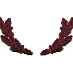 May include: Two maroon fabric leaf wreaths, each with three leaves, are shown against a white background.