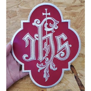 May include: Red felt patch with a white embroidered monogram of "IHS" with a cross above the "I".