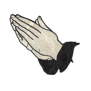 May include: Embroidered patch featuring hands clasped in prayer. The hands are a light beige color with black outlines and details. The cuffs are black. The patch is designed to be ironed on or sewn onto fabric.