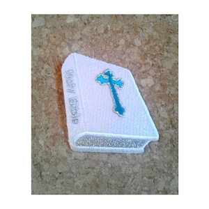 May include: White embroidered patch with a silver outline depicting a closed book with the words "Holy Bible" on the spine and a teal cross on the front.