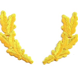 May include: Two gold embroidered laurel wreaths, each with five leaves, are arranged in a symmetrical design.