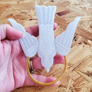 May include: White embroidered dove with outstretched wings, descending into a gold ring. The dove is a symbol of peace and the Holy Spirit.