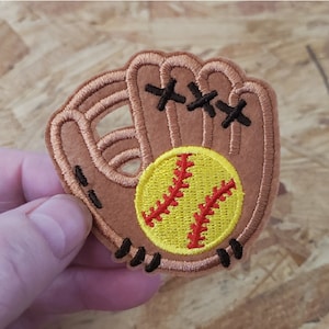 May include: A brown felt softball glove with red and yellow stitching, holding a yellow softball with red stitching.