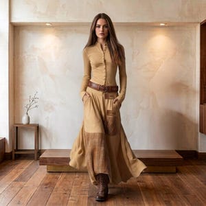 Könnte beinhalten: Ein beigefarbenes Kleid mit langen Ärmeln, einem durchgehenden Knopfverschluss am Oberteil, einem braunen Ledergürtel in der Taille und einem langen Rock mit einem karierten Einsatz sowie einer rechteckigen aufgesetzten Tasche, kombiniert mit braunen Stiefeln.
