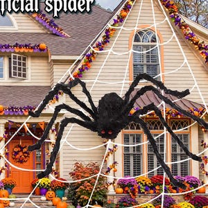 May include: A large black artificial spider with red eyes positioned on a white web, displayed on the front of a house decorated for Halloween with orange pumpkins, purple and orange garlands, and the text Halloween Artificial spider.
