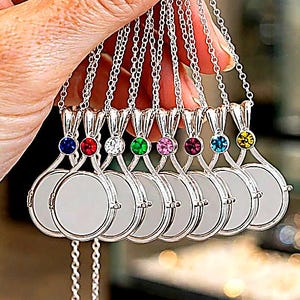 May include: A collection of silver-toned necklaces featuring circular pendants with blank white centers. Each pendant is topped with a small, colored gemstone in shades of blue, red, clear, green, pink, magenta, turquoise, and yellow.