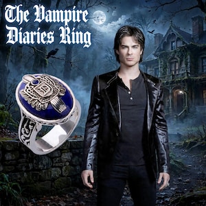 May include: A silver ring featuring a deep blue oval stone and an ornate metal crest with the letter D. The ring is displayed against a background showing a person in a black jacket and a dark house with the text The Vampire Diaries Ring.