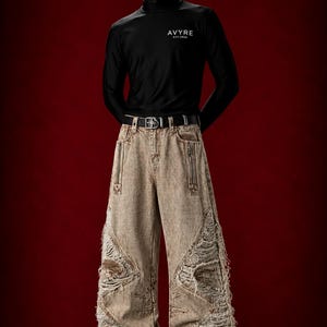 May include: A black long-sleeve shirt with the white text AVYRE EST.2026 on the chest and a black mask with the same text. The shirt is paired with wide-leg, distressed tan denim jeans featuring zippered pockets, frayed panels, and white sneakers.