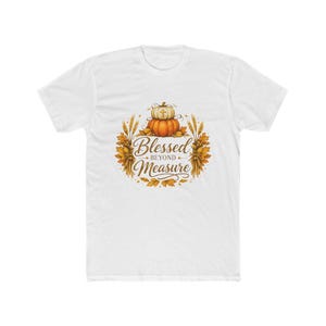 May include: A white short-sleeve t-shirt featuring a central graphic of two stacked pumpkins, one orange and one white with a small cross, surrounded by wheat stalks and autumn leaves, with the text Blessed BEYOND Measure in brown script.