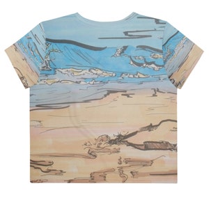 Könnte beinhalten: Ein blaues und beiges T-Shirt mit einem Aquarell-Design einer Strandszene. Das Design zeigt Wellen, Sand und einen Himmel mit Wolken.