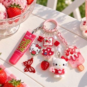 Può includere: Un portachiavi rosa con un tubetto di lucidalabbra Essence Chili Bomb, una statuetta di Hello Kitty, un ciondolo a forma di ghiacciolo alla fragola, una farfalla rossa, un fungo e un piccolo cuscino quadrato con grafiche di fragole.