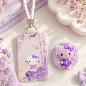 Puede incluir: Un porta credenciales rectangular de color morado con una correa de muñeca trenzada blanca y un soporte circular para teléfono a juego, ambos con un diseño de Hello Kitty con lazo morado, suéter morado y fondo de tallos de bambú morados.