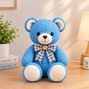 May include: A crocheted teddy bear in bright blue yarn with white accents on the ears and feet. The bear features black plastic eyes, a brown stitched nose, and a blue and beige checkered bow tie secured with a small wooden button at the neck.