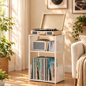 May include: A white metal two-tier storage stand with mesh side panels. The top shelf holds a beige portable suitcase-style record player and a small speaker. The bottom shelf contains a collection of vinyl records organized with metal dividers.