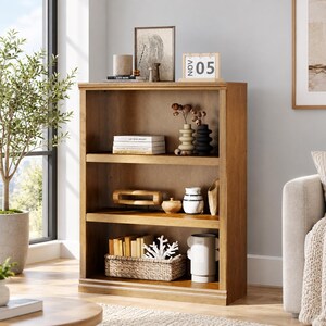 May include: A medium-toned wooden bookcase with three open shelves. The top shelf holds books, a textured vase, and a black vase. The middle shelf contains a wooden sculpture, a small bowl, and a patterned vase. The bottom shelf features a woven basket with books and a white coral-like object, alongside a white cylindrical vase.