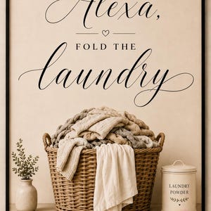 May include: A framed wall art print featuring the black text Alexa, FOLD THE laundry with a small heart icon. Below the text is a woven wicker basket overflowing with folded beige and grey knit blankets and a white cloth, a small vase, and a canister.