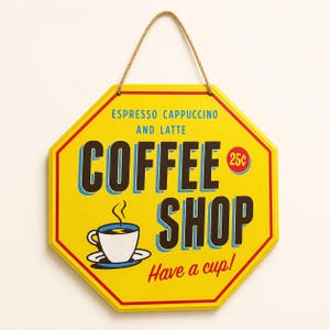 Peut inclure: Une enseigne murale octogonale jaune avec une cordelette en jute. Elle présente le texte "COFFEE SHOP", "ESPRESSO CAPPUCCINO AND LATTE", "25¢" et "Have a cup!" ainsi qu'un graphique d'une tasse de café blanche fumante sur une soucoupe.