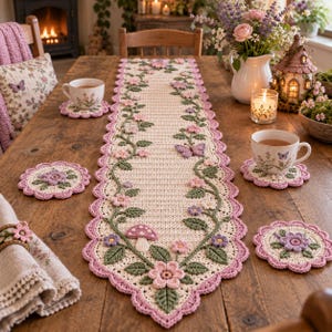 Peut inclure: Un chemin de table en crochet couleur crème avec une bordure festonnée rose, des vignes vertes, des fleurs roses et violettes, un petit champignon et un papillon. L'ensemble comprend quatre dessous de verre assortis et un rond de serviette.