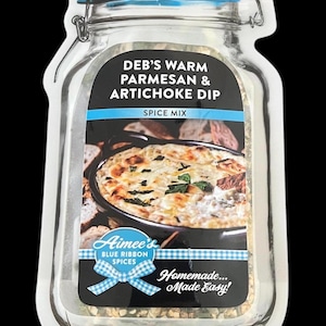 May include: Aimee's Blue Ribbon Spices Deb's Warm Parmesan & Artichoke Dip Spice Mix. A clear glass jar with a blue lid and a white label with a picture of a dip in a black bowl. The label says "Homemade... Made Easy!"