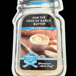 May include: Aimee's Blue Ribbon Spices jar with a white label and blue ribbon design. The label reads "For the Love of Garlic Butter Spice Mix" and "Homemade... Made Easy!" The jar is filled with a light brown spice mix and a photo of garlic butter on bread is on the label.