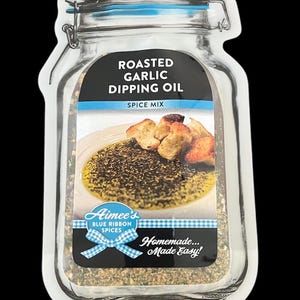 May include: A clear glass jar with a blue lid and a white label that says "Roasted Garlic Dipping Oil Spice Mix". The label also has a picture of a bowl of dipping oil with bread.