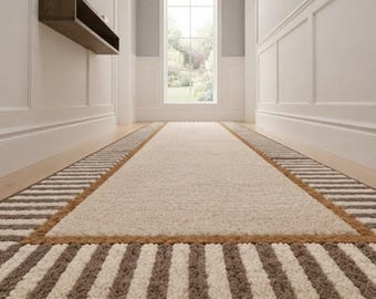 May include: A rectangular runner rug featuring a solid cream-colored center bordered by a textured frame of alternating brown and cream stripes. The rug has a thick, tufted pile construction and is positioned lengthwise on a wooden floor.