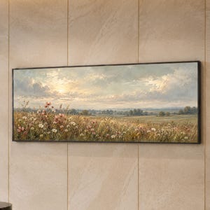 Könnte beinhalten: Ein rechteckiges Landschaftsgemälde in einem dünnen schwarzen Rahmen, das ein Feld mit Wildblumen unter einem weichen, bewölkten Himmel bei Sonnenuntergang zeigt. Die Szene umfasst goldene Gräser, weiße und rosa Blüten sowie ferne Bäume.