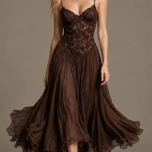 May include: A dark brown midi dress featuring a fitted bodice with intricate floral lace detailing and thin spaghetti straps. The skirt is constructed from a lightweight, pleated fabric that flares out from the waist, ending in a ruffled hemline.