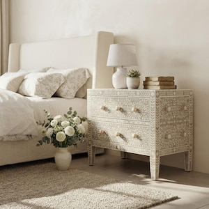 Puede incluir: Una mesita de noche rectangular de dos cajones con un intrincado patrón floral incrustado en gris claro y blanco. La pieza cuenta con cuatro patas rectas y pequeños pomos de madera clara en cada cajón, ofreciendo una superficie de almacenamiento.