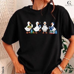 Könnte beinhalten: Ein schwarzes T-Shirt mit einer Grafik von vier weißen Enten. Die erste Ente isst einen Salat, die zweite hält ein Blutzuckermessgerät, die dritte hält ein Klemmbrett mit der Aufschrift Diabetes Plan und die vierte liest ein Buch Diabetes Life.