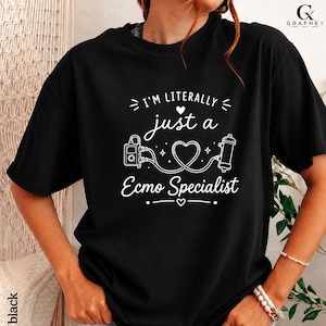 Könnte beinhalten: Ein schwarzes Kurzarm-T-Shirt mit weißem Grafiktext, der I'M LITERALLY just a Ecmo Specialist lautet. Das Design enthält eine zentrale Herzform, die mit Symbolen für medizinische Geräte, kleinen Sternen und dekorativen Linien verbunden ist.