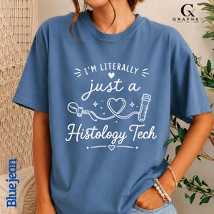 Könnte beinhalten: Ein blaues T-Shirt mit weißem Aufdruck, der den Text I'M LITERALLY just a Histology Tech zeigt. Das Design enthält eine durchgehende Linienzeichnung eines Herzens, eines Labor-Reagenzglases und eines medizinischen Objektträgerhalters.