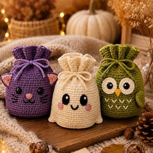 May include: Three small, round, crocheted drawstring pouches featuring animal-inspired designs. The left pouch is purple with cat ears, the center pouch is cream with a smiling face, and the right pouch is olive green with owl features.