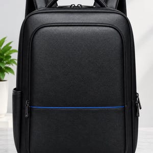Puede incluir: Una mochila negra con acabado texturizado, que cuenta con un asa superior, correas acolchadas para los hombros y una línea de acento azul horizontal en el bolsillo frontal. La bolsa incluye cremalleras dobles y bolsillos laterales.