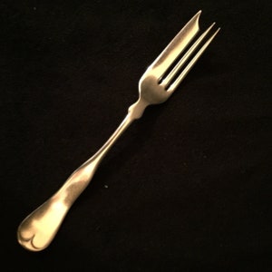 May include: A silver fork with a decorative handle and three tines. The fork is on a black background.